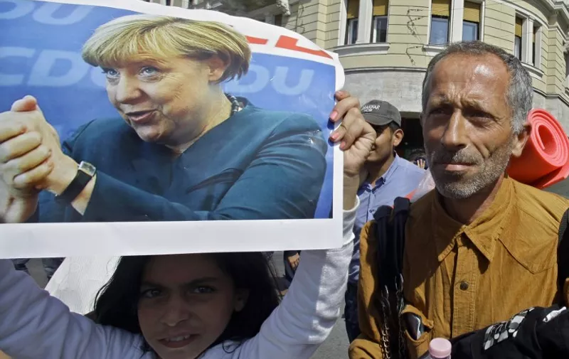 A migrant girl holds a poster of German Chancellor Angela Merkel as migrants walk in Budapest downtown after leaving the transit zone of the main train station, on September 4, 2015 intenting on walking to the Austrian border. They were part of an estimated 2,000 migrants stuck in makeshift refugee camps at Keleti station, after railway authorities had blocked them from boarding trains to Austria and Germany. AFP PHOTO / PETER KOHALMI