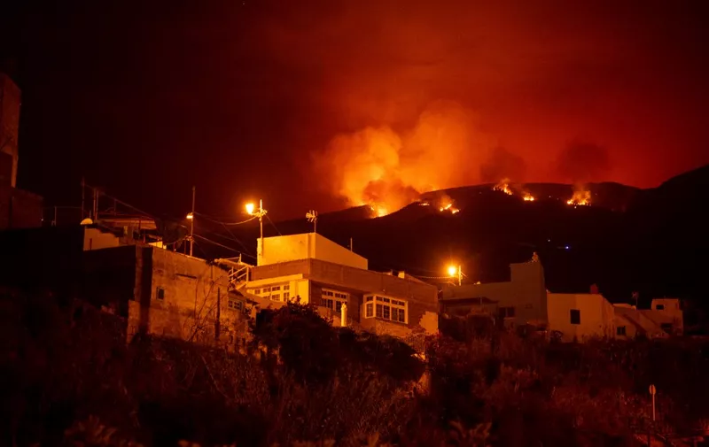 A picture taken in the night of August 19, 2023 shows the fronts of the forest fire on hills above houses, in the Guimar valley on the Canary Island of Tenerife. The blaze, which officials say is the most "complex fire" to hit the Canary Islands in 40 years, broke out on August 15 in a mountainous area of northeastern Tenerife. 225 firefighters are struggling against the ferocious blaze which has so far destroyed nearly 5,000 hectares (more than 12,000 acres) of land, has a perimeter of 50 kilometres (30 miles) and led to the evacuation and/or confinement of some 7,600 people from nine population centers. (Photo by DESIREE MARTIN / AFP)