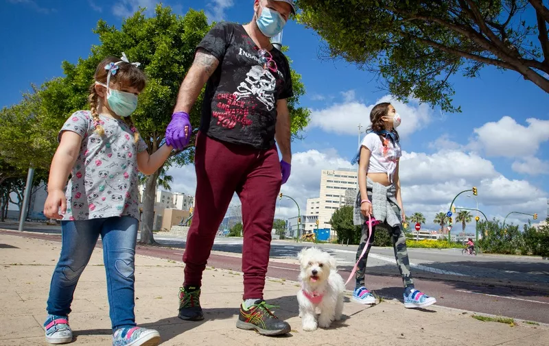 Two girls walk their dog with their father in Palma de Mallorca, on April 26, 2020 during a national lockdown to prevent the spread of the COVID-19 disease. - After six weeks stuck at home, Spain's children were being allowed out today to run, play or go for a walk as the government eased one of the world's toughest coronavirus lockdowns. Spain is one of the hardest hit countries, with a death toll running a more than 23,000 to put it behind only the United States and Italy despite stringent restrictions imposed from March 14, including keeping all children indoors. Today, with their scooters, tricycles or in prams, the children accompanied by their parents came out onto largely deserted streets. (Photo by JAIME REINA / AFP)