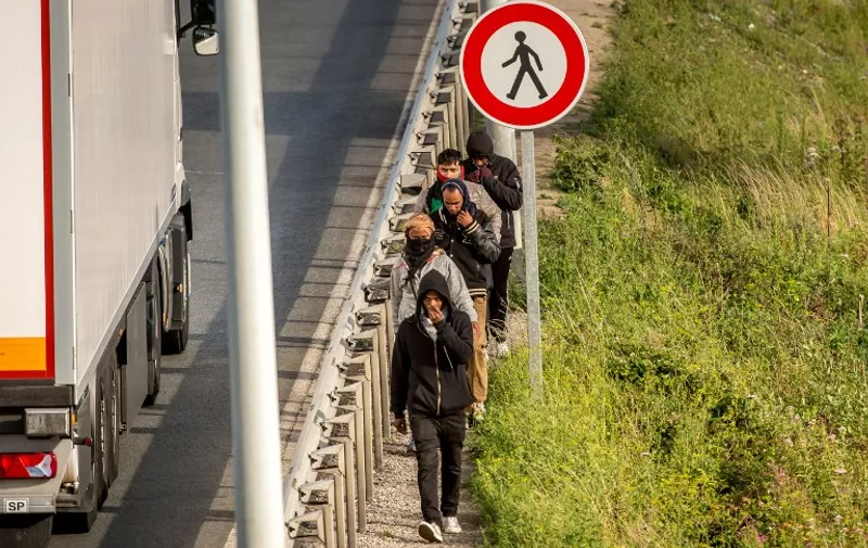 Migrants walk alongside vehicles on the route leading to the Eurotunnel in Coquelles on July 29, 2015.   One man died in a desperate attempt to reach England via the Channel Tunnel as overwhelmed authorities fought off hundreds of migrants, prompting France to beef up its police presence. British ministers convened for emergency talks on the mounting crisis, as Prime Minister David Cameron acknowledged the situation in the northern French city of Calais was "very concerning."  AFP PHOTO / PHILIPPE HUGUEN