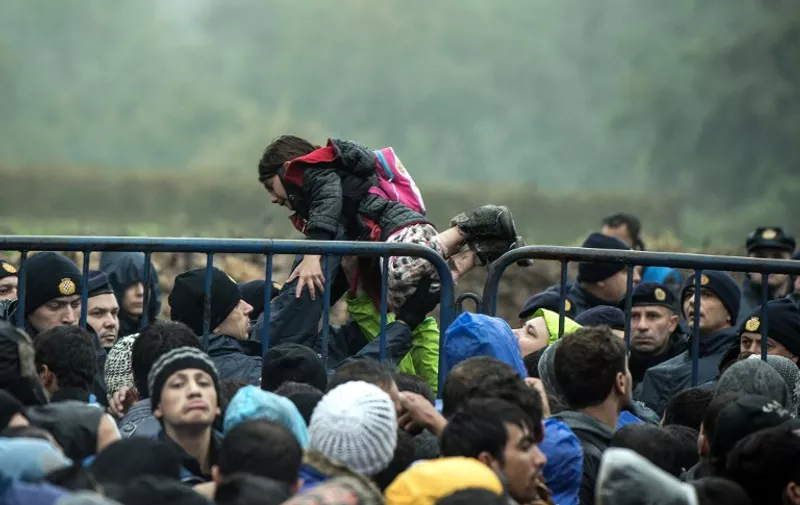 A Croatian police officer carries a child as migrants wait to enter Croatia from the Serbia-Croatia border, near the western Serbian village of Berkasovo, on October 19, 2015. Long lines have formed on Croatia's border with Serbia. Several hundred people remained stuck there on October 19 morning, after having spent the night in rain and cold weather. Earlier on OCtober 18, 2015, migrants were forced to sit for several hours in about 50 buses stuck in Serbia near the border after Croatia stopped allowing any crossings. They later resumed, but at a much slower pace than before. AFP PHOTO / ANDREJ ISAKOVIC