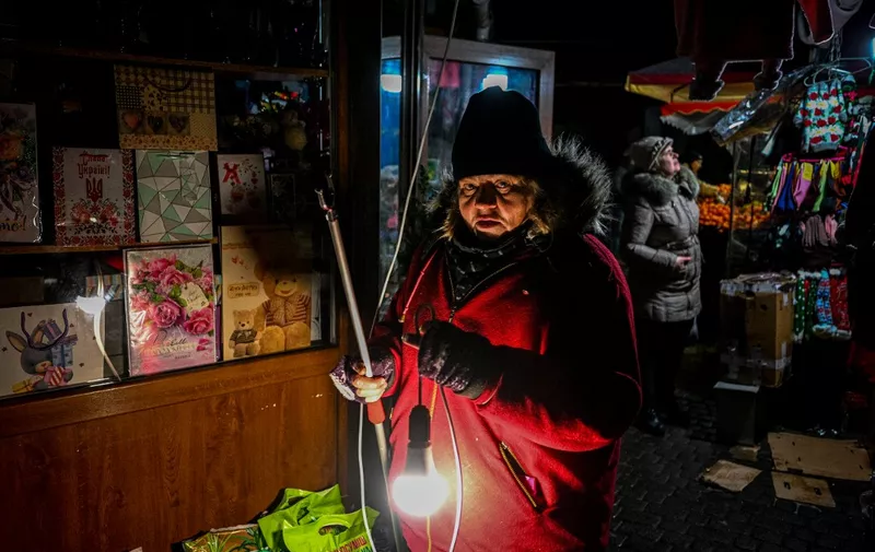 A vendor waits for customers during a blackout at a market in the Western Ukrainian city of Lviv on December 15, 2022, amid the Russian invasion of Ukraine. - With temperatures dipping below zero, repeated Russian attacks have left Ukraine's energy grid teetering on the brink of collapse and have disrupted power and water supplies to millions over recent weeks. (Photo by YURIY DYACHYSHYN / AFP)