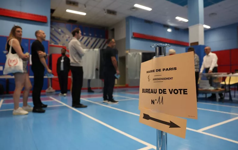 This photograph shows a sign indicating the polling station as voters stand in line during the second round of France's legislative election at a polling station in Paris on July 7, 2024. France votes in legislative elections on July 7, 2024 that will be decisive in determining its political future and could see the far right become the largest party in parliament for the first time. (Photo by EMMANUEL DUNAND / AFP)