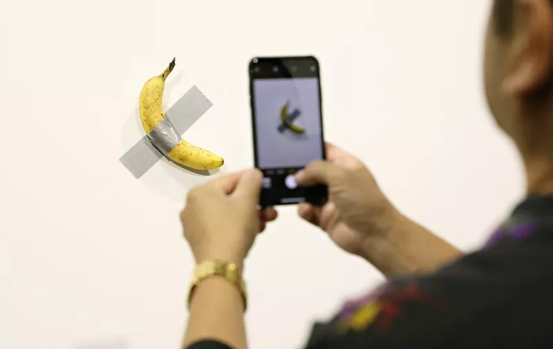 MIAMI BEACH, FL - DECEMBER 06: People post in front of Maurizio Cattelan's "Comedian" presented by Perrotin Gallery and on view at Art Basel Miami 2019 at Miami Beach Convention Center on December 6, 2019 in Miami Beach, Florida. Two of the three editions of the piece, which feature a banana duct-taped to a wall, have reportedly sold for $120,000.   Cindy Ord/Getty Images/AFP (Photo by Cindy Ord / GETTY IMAGES NORTH AMERICA / Getty Images via AFP)