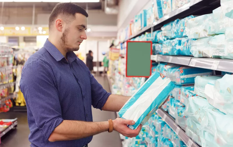 man with diaper pack in supermarket reading product information.