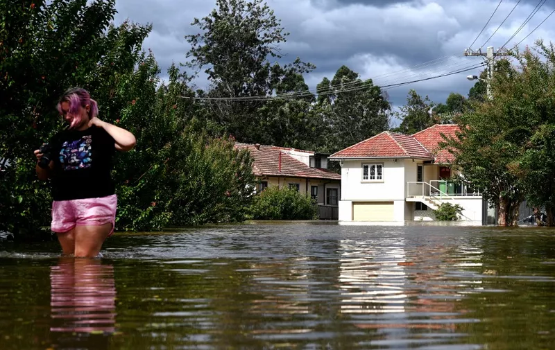 A woman (L) wades through water near inundated homes along the overflowing Hawkesbury River in the Windsor suburb of Sydney on March 9, 2022. (Photo by SAEED KHAN / AFP)