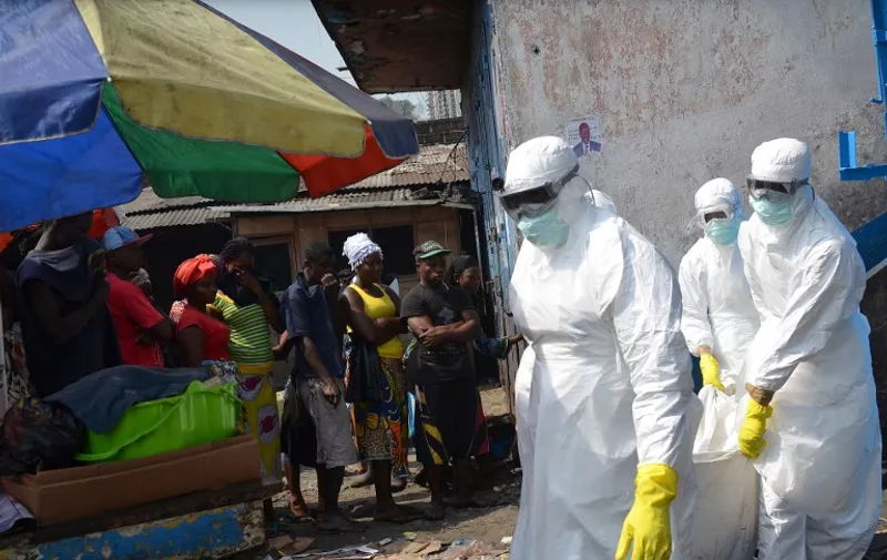 (FILES) A file picture taken on January 5, 2015 shows red cross workers, wearing protective suits, carrying the body of a person who died from Ebola during a burial with relatives of the victims of the virus, in Monrovia. Liberia announced the return of the deadly Ebola virus on Tuesday, more than six weeks after the country eradicated the disease. AFP PHOTO / ZOOM DOSSO