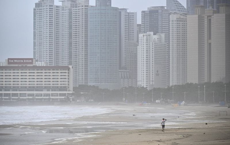 A man walks along a beach during winds brought on by Typhoon Khanun at the southeastern port city of Busan on August 10, 2023. (Photo by Anthony WALLACE / AFP)