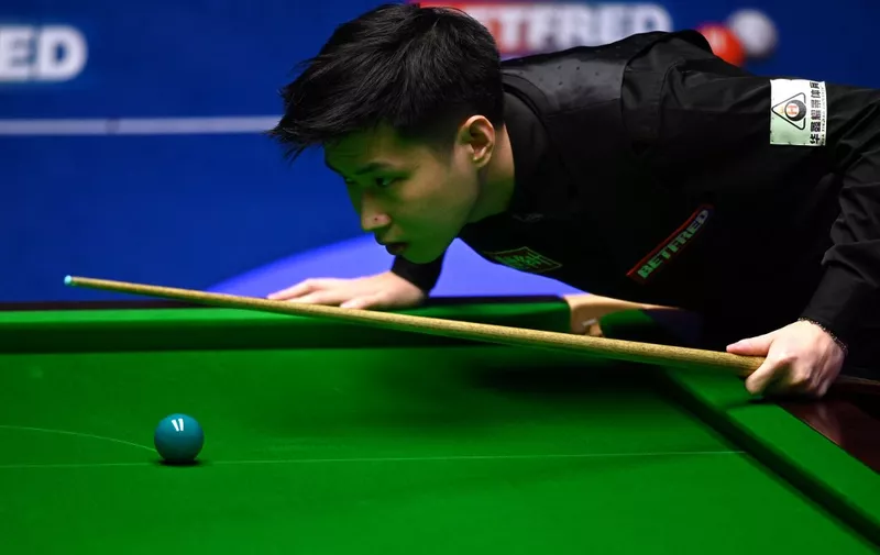 China's Zhao Xintong leans over the table while playing against Scotland's Stephen Maguire during their World Championship Snooker second round match at The Crucible in Sheffield, England on April 22, 2022. (Photo by Oli SCARFF / AFP)