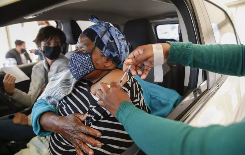 A woman receives a second dose of the Pfizer Covid-19 vaccine from a healthcare worker while her employer looks on at the Zwartkops Raceway in Centurion on August 13, 2021. (Photo by Phill Magakoe / AFP)