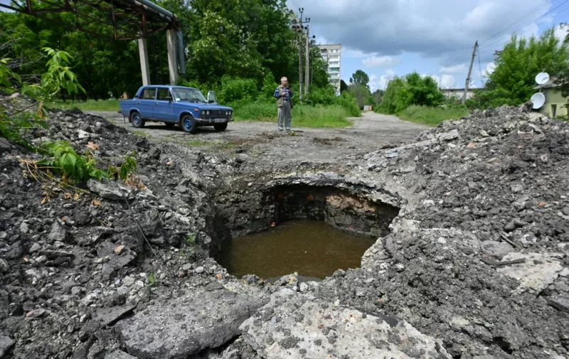 A local resident looks on next to a crater in the centre of Kupiansk, Kharkiv region, on May 26, 2023, amid the Russian invasion of Ukraine. (Photo by SERGEY BOBOK / AFP)
