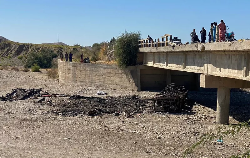 Residents gather over a bridge to watch the wreckage of a burnt passenger bus in Lasbela district of Pakistan's Balochistan province on January 29, 2023. - At least 40 people died when a bus plunged off a bridge in southwestern Pakistan and burst into flames, a government official said on January 29. (Photo by Ismail Sasoli / AFP)