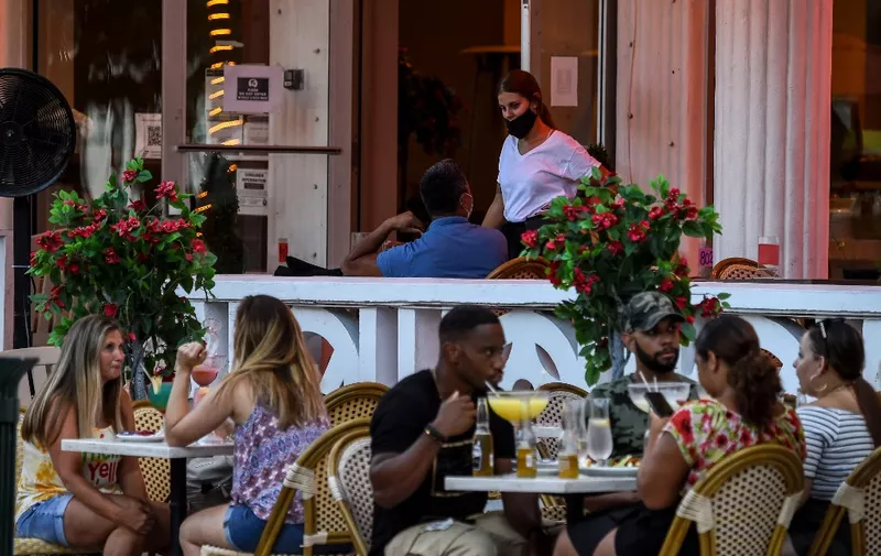 A waiter takes orders from customers at a restaurant on Ocean Drive in Miami Beach, Florida on July 14, 2020, amid the coronavirus pandemic. - The US state of Florida -- one of the current epicenters in the nation's coronavirus crisis -- on Tuesday posted a record number of deaths for a 24-hour period at 132. The state department of health announced the grim milestone in its daily statistics on the virus pandemic. It reported more than 9,000 new cases in the same 24-hour span. (Photo by CHANDAN KHANNA / AFP)