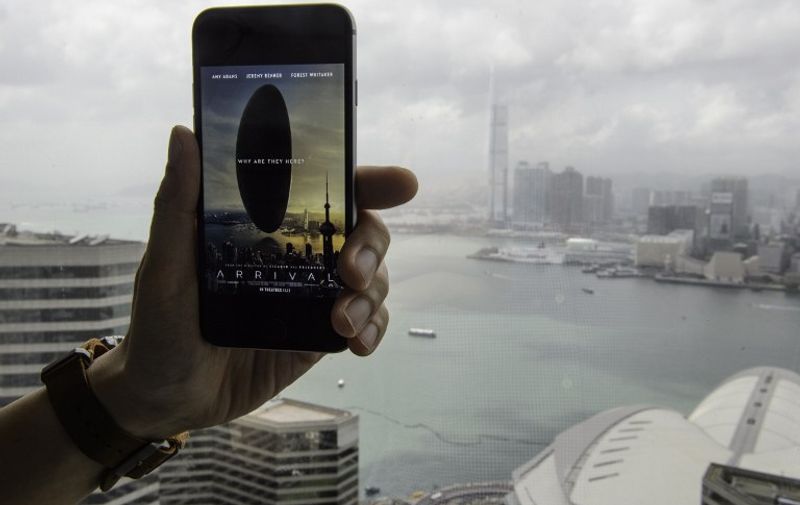 This photo illustration taken on August 19, 2016 shows a smartphone user holding up his device displaying the pulled theatrical release poster for the film "Arrival" - which depicts a giant spaceship over Hong Kong's Victoria Harbour with Shanghai's landmark Oriental Pearl Tower in the poster's right foreground - as the harbour skyline is seen from the observation deck of a skyscraper in Hong Kong's Wanchai district.
A poster for upcoming Hollywood movie "Arrival" mistakenly featuring a Shanghai landmark on Hong Kong's skyline was taken down from the film's official Facebook page on August 19 after sparking outrage and ridicule. / AFP PHOTO / TENGKU BAHAR