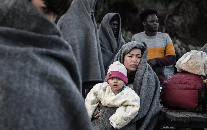 Migrants and refugees who arrived from Turkey to the Greek island of Lesbos on March 5, try to keep warm as they gather in the yard of a small church where they have spent the rainy night near Skala Sykamnias on March 6, 2020. - A group of 42 refugees and migrants weave through coast guard patrols and arrived on the shores of Lebos during the evening of March 5. (Photo by LOUISA GOULIAMAKI / AFP)