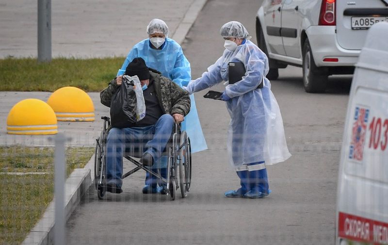 Medical workers wearing personal protective equipment (PPE) push a patient in a wheelchair towards the entrance of a hospital in Kommunarka on the outskirts of Moscow on November 16, 2020, amid the ongoing coronavirus (Covid-19) pandemic. (Photo by NATALIA KOLESNIKOVA / AFP)