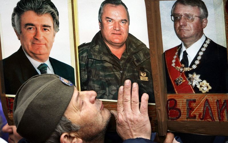 A Serbian Radical party supporter kisses photos of war crimes suspects Radovan Karadzic (L), Ratko Mladic (C) and Vojislav Seselj (R) at the party rally in Belgrade, 24 February 2006. Radovan Karadzic and Radko Mladic are the most wanted war crimes fugitives, while Vojislav Seselj has been detained at the UN tribunal in The Hague for three years, pending trial. A Serbian ultranationalist party on Thursday urged fugitive Bosnian Serb general Ratko Mladic not to surrender to the UN warcrimes court, despite mounting pressure on Belgrade to hand over one of the most wanted suspects of the Balkan wars in 1990s.       AFP PHOTO / DIMITAR DILKOFF (Photo by DIMITAR DILKOFF / AFP)