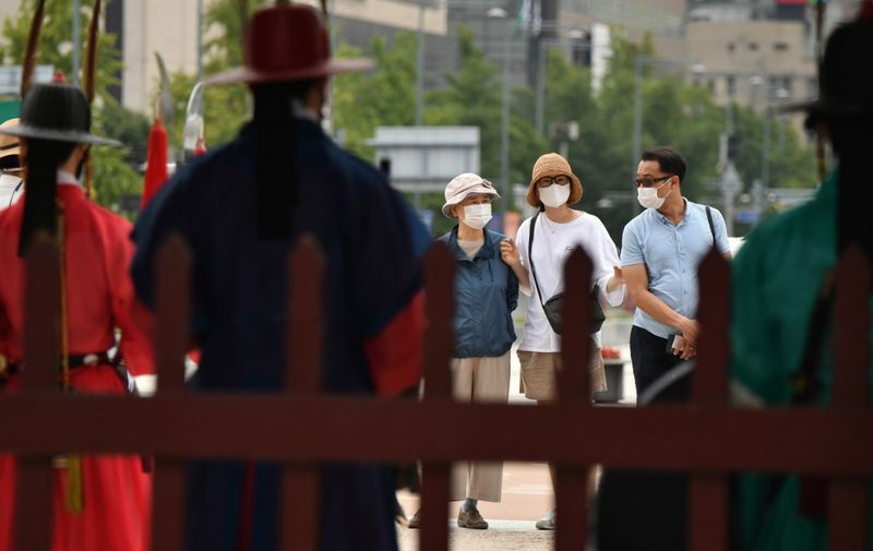 Visitors wearing face masks look at costumed royal guards performing for tourists at Gyeongbokgung Palace in Seoul on September 14, 2020. - South Korea will temporarily ease coronavirus curbs in the greater Seoul area after a decline in cases, officials said on September 13. The country largely overcame an early Covid-19 surge with extensive tracing and testing, but has battled several spikes in recent weeks raising concerns of a second wave of infections. (Photo by Jung Yeon-je / AFP)