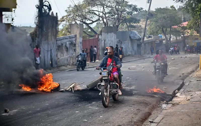 People ride motorbikes past burning tires during a demonstration calling for the resignation of Prime Minister Ariel Henry, in Port-au-Prince, Haiti, on February 6, 2024. Haitis government on February 5, 2024 announced a crackdown on the para-military and environtmental agency Protected Areas Security Brigade (BSAP) whose heavily armed agents have gained power recently and have been blamed for violent clashes with police last week. (Photo by Richard PIERRIN / AFP)