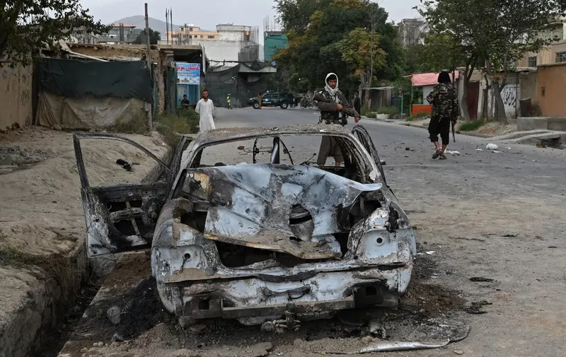 Taliban fighters stand guard near a damaged car after multiple rockets were fired in Kabul on August 30, 2021. - Rockets flew across the Afghan capital on August 30 as the US raced to complete its withdrawal from Afghanistan, with the evacuation of civilians all but over and terror attack fears high. (Photo by WAKIL KOHSAR / AFP)