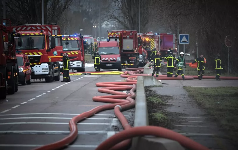 Firefighters stand in a street after battling an overnight fire at an industrial building belonging to Bollore Logistics, in Grand-Couronne, south of Rouen, on January 17, 2023. - A Bollore Logistics industrial warehouse housing lithium batteries caught fire, sparking an emergency operation manned by around 100 firefighters and 30 vehicles, reports head of Seine-Maritime fire service press relations head Guillaume Casada. (Photo by Lou BENOIST / AFP)