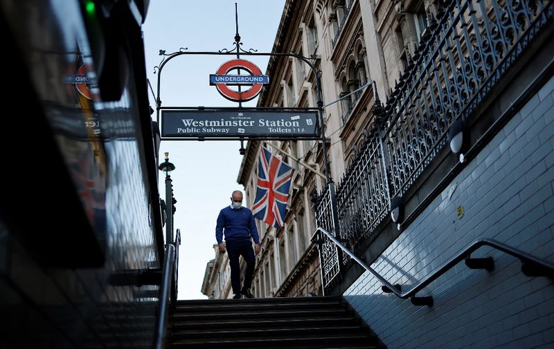 A member of the public wearing a face covering to mitigate the spread of Covid-19, walks beneath a Union flag as he enters Westminster Station in central London on January 5, 2022. - British hospitals have switched to a "war footing" due to staff shortages caused by a wave of Omicron infections, the government said Tuesday, as the country's daily Covid caseload breached 200,000 for the first time. (Photo by Tolga Akmen / AFP)