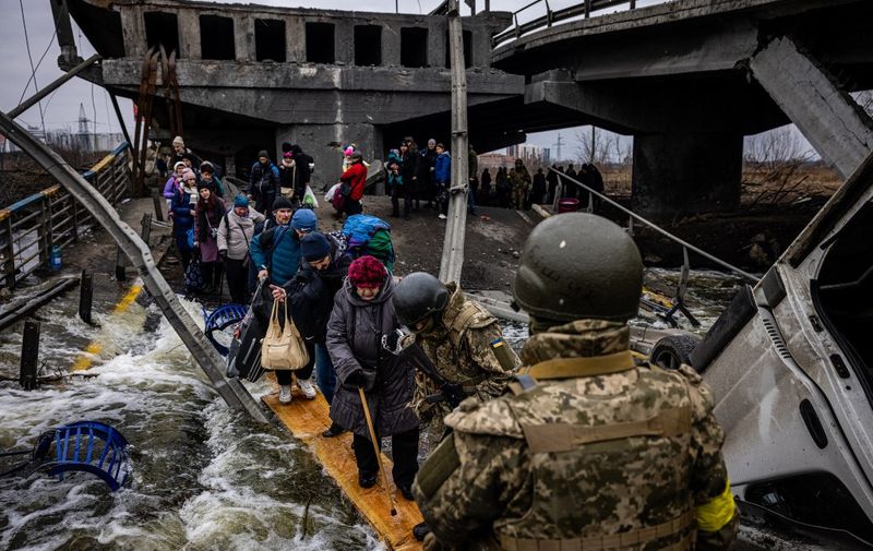 Evacuees cross a destroyed bridge as they flee the city of Irpin, northwest of Kyiv, on March 7, 2022. - Ukraine dismissed Moscow's offer to set up humanitarian corridors from several bombarded cities on Monday after it emerged some routes would lead refugees into Russia or Belarus. The Russian proposal of safe passage from Kharkiv, Kyiv, Mariupol and Sumy had come after terrified Ukrainian civilians came under fire in previous ceasefire attempts. (Photo by Dimitar DILKOFF / AFP)