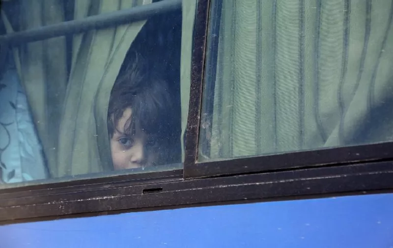 A Syrian child evacuated from Eastern Ghouta looks out from the window of a bus after arriving in Qalaat al-Madiq, some 45 kilometres northwest of the central city of Hama, on March 30, 2018, following the ongoing evacuation deals made between rebel fighters and Russia, an ally of the Syrian President. / AFP PHOTO / Zein Al RIFAI