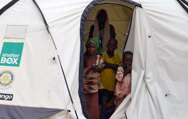 A picture taken on September 16, 2015 shows children standing in a tent in the Assaga refugee camp,  set up by the UN three months ago for Nigerian refugees who fled to southeast Niger to escape the Islamist group Boko Haram. In the Assaga camp, many refugees live in abject poverty and sleep in makeshift shelters at the mercy of mosquitoes and bad weather, an AFP reporter saw. AFP PHOTO / BOUREIMA HAMA
