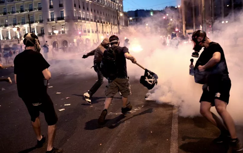 Protesters clash with riot police in front of the Greek Parliament in Athens on July 15, 2015 during an-anti-austerity protest. Anti-austerity protesters hurled petrol bombs at police in front of Greece's parliament on July 15 as lawmakers began debating unpopular reforms needed to unlock a new eurozone bailout.Riot police responded with tear gas against dozens of hooded protesters who set ablaze parts of Syntagma square in central Athens AFP PHOTO / ANGELOS TZORTZINIS
