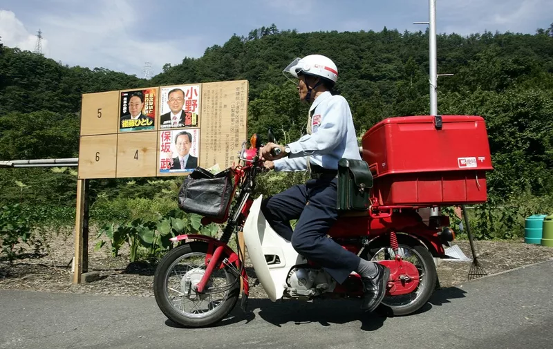 Riding the red postal motorbike, a postman runs past a posters of candidates for 11 September lower house elections to deliver mails and percels in Hayakawa, 160 kilometers (100 miles) west of Tokyo, 02 September 2005.  The post office have taken deep root in Japanese communities over more than 130 years and its diverse role is all the more important for villagers because of their rapidly greying society.     AFP PHOTO/Toru YAMANAKA (Photo by TORU YAMANAKA / AFP)