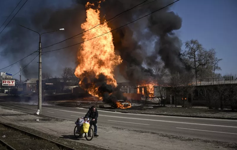 A man flees with his belongings as fire engulfs a vehicle and building following artillery fire on the 30th day of the invasion of Ukraine by Russian forces, in the northeastern city of Kharkiv on March 25, 2022. - Russian strikes targeting a medical facility in Ukraine's second city of Kharkiv on March 25, 2022, killing at least four civilians and wounding several others, Ukrainian officials said. (Photo by Aris Messinis / AFP)