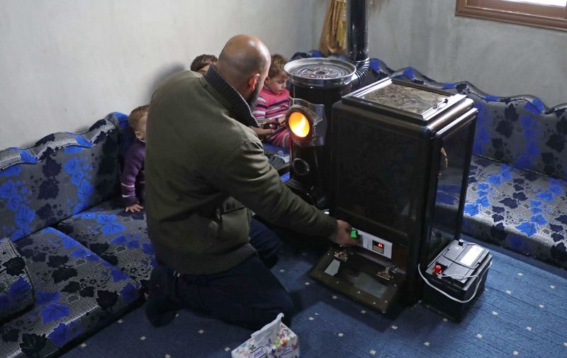 Abu Walid adjusts the temperature of a pistachio-powered heater with a dial regulating the number of shells burned per minute, in his living room in Tal al-Karama village in Syria's northwestern province of Idlib on December 6, 2019. - In recent months, Syria has suffered a fuel crisis that has seen a spike in the price of heating oil and long queues for much-demanded cooking gas in government-held parts of the country. The rising cost of heating fuel has made warm homes a luxury in a province where unemployment is high and public services are non-existent. (Photo by Aaref WATAD / AFP)