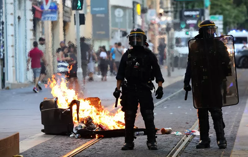 French riot police officers stand guard next to a burnt out trash bin during a demonstration against police in Marseille, southern France on July 1, 2023, after a fourth consecutive night of rioting in France over the killing of a teenager by police. French police arrested 1311 people nationwide during a fourth consecutive night of rioting over the killing of a teenager by police, the interior ministry said on July 1, 2023. France had deployed 45,000 officers overnight backed by light armoured vehicles and crack police units to quell the violence over the death of 17-year-old Nahel, killed during a traffic stop in a Paris suburb on June 27, 2023. (Photo by CLEMENT MAHOUDEAU / AFP)