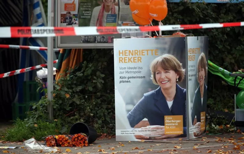Flowers are layed next to an election campaign poster of the candidate for mayor's election Henriette Reker near the place where she was attacked by a man in Cologne, western Germany, on October 17, 2015. The crossbench candidate Henriette Reker was stabbed by a man and seriously injured while canvassing on the eve of the elections. AFP PHOTO / DPA / OLIVER BERG GERMANY OUT