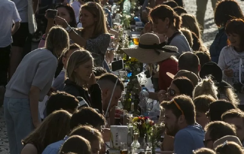 People walk past and sit at a half-kilometre long table set up on the Charles Bridge in Prague to celebrate the end of the restrictions linked to the new coronavirus pandemic on June 30, 2020. - Some 2,000 seats are proposed with people being invited to bring and share food. (Photo by Michal Cizek / AFP)