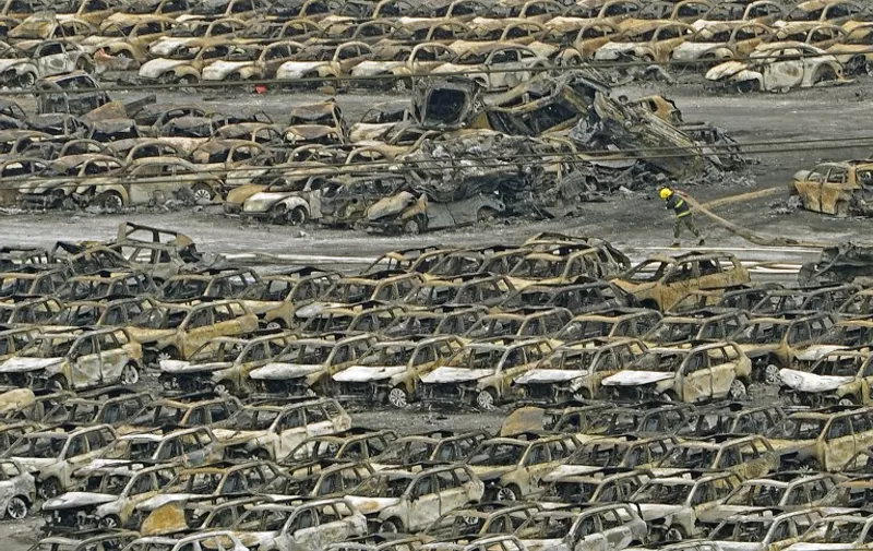 TOPSHOTS
This photo taken on August 14, 2015 shows a firefighter walking past damaged cars at the site of the explosions in Tianjin.  Residents near the site of two giant explosions in the northern Chinese port city of Tianjin were being evacuated on August 15 over fears of toxic contamination, the official Xinhua news agency said. CHINA OUT     AFP PHOTO