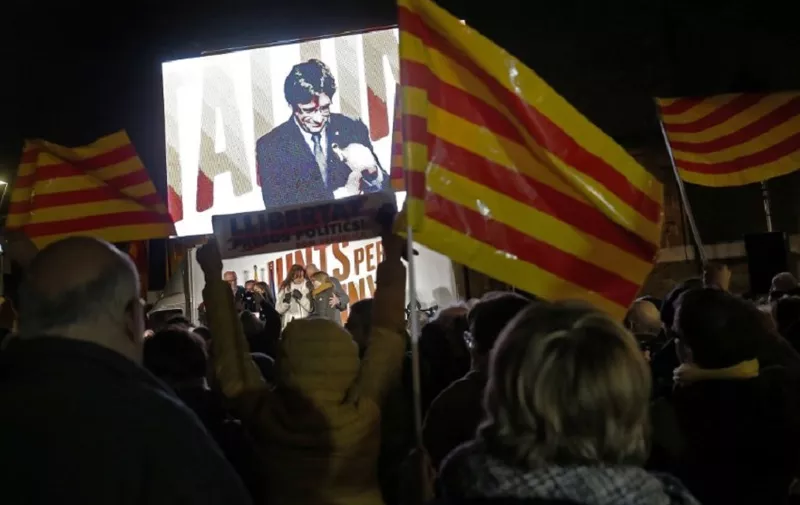People wave flags and hold banners demanding freedom for jailed separatists leaders as they watch deposed Catalan regional president and 'Junts per Catalonia' - JUNTSXCAT (All for Catalonia) grouping candidate Carles Puigdemont speaking via video-conference from Brussels during the final campaign meeting for the upcoming Catalan regional election on December 19, 2017 in Barcelona. 
Catalan voters will decide on December 21 whether to return the separatists to power or to bring in a pro-unity government, as their region's independence crisis nears its moment of truth. / AFP PHOTO / Pau Barrena
