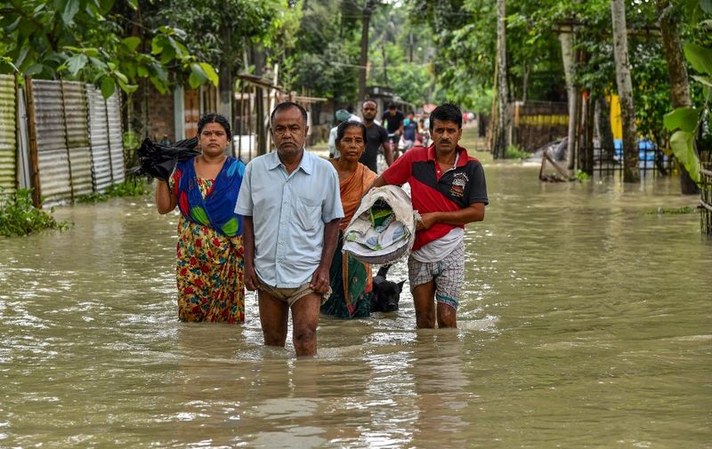 People wade through flood waters in Solmara of Nalbari district, in India's Assam state on June 19, 2022. (Photo by Biju BORO / AFP)