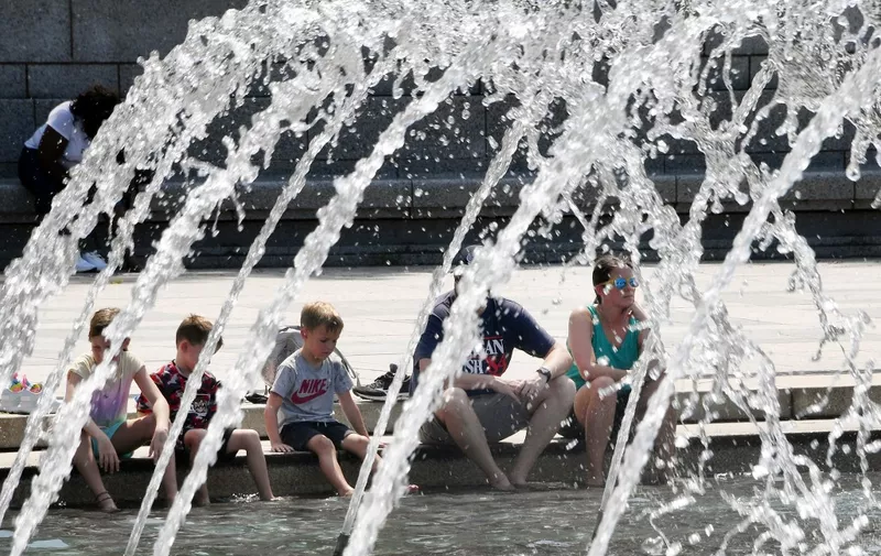 People put their feet in the water at the National World War II Memorial on the National Mall in Washington, DC, August 12, 2021, as a heat wave continues in the area, with the National Weather Service issuing a heat advisory for extreme temperatures and high humidity. (Photo by Olivier DOULIERY / AFP)