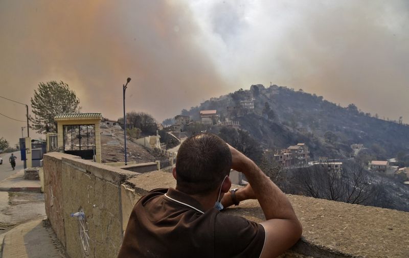 A man looks on as smoke rises from a wildfire in the forested hills of the Kabylie region,  east of the capital Algiers, on August 10, 2021. - At least five people have died in raging wildfires in Algeria as firefighters battle more than 31 blazes amid blistering temperatures and tinder-dry conditions, officials said. (Photo by Ryad KRAMDI / AFP)