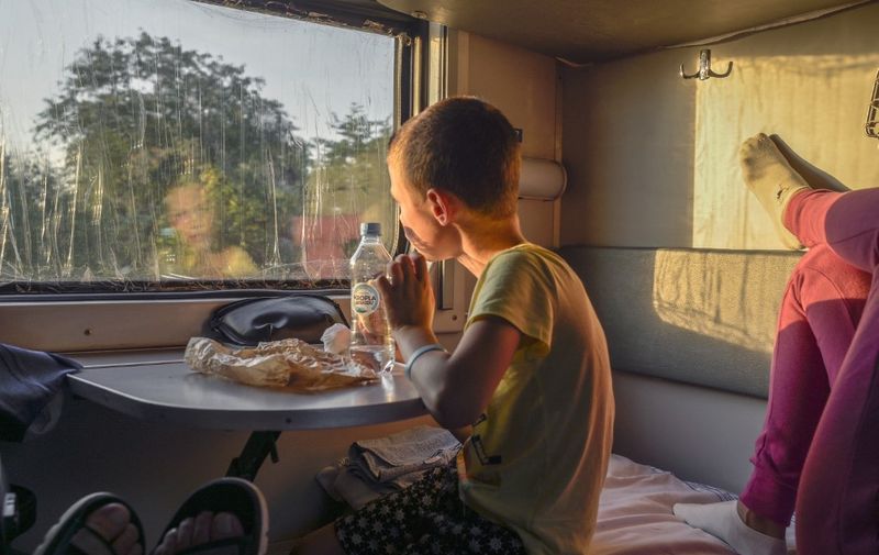 Artem, 8, watches outside near his mother in a night train on its way to Odessa near the Polish and Ukrainian border near Przemsyl, on July 19, 2022. - Natasha and her son Artem took a night train to come back from Poland their home, located some 40 kilometres away in the north of Odessa. (Photo by BULENT KILIC / AFP)