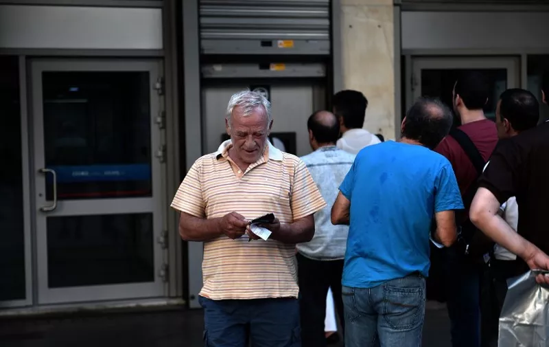 People queue outside a bank to withdraw cash from an ATM in Athens on July 7, 2015. Eurozone leaders will hold an emergency summit in Brussels on July 7 to discuss the fallout from Greek voters' defiant "No" to further austerity measures, with the country's Prime Minister Alexis Tsipras set to unveil new proposals for talks.  European Commission head Jean-Claude Juncker said on July 7 that he was against an exit by Greece from the euro, even though Greeks massively rejected bailout terms in a referendum two days prior. AFP PHOTO / ARIS MESSINIS