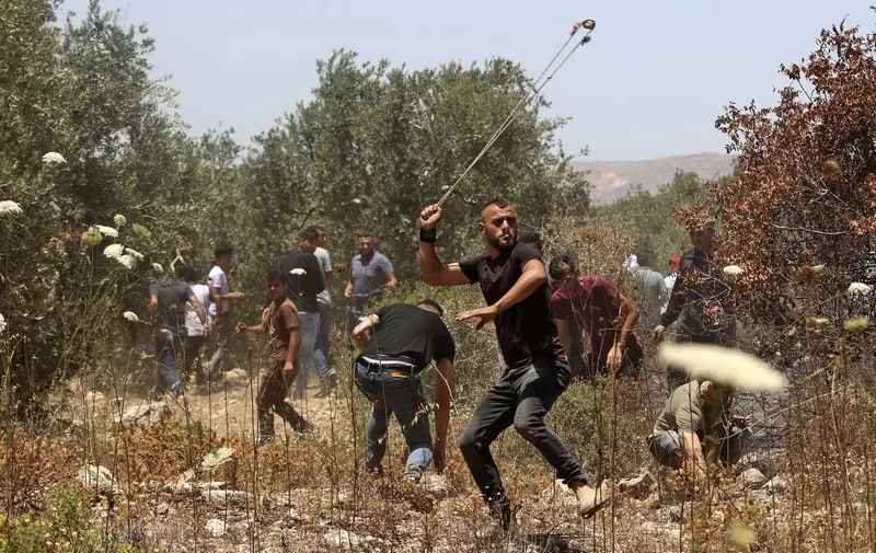 Palestinian protesters use slingshots to hurl stones at Israeli security forces amid clashes in the village of Baita, south of Nablus, in the occupied West Bank on May 28, 2021, following a demonstration against the establishment of Israeli outposts in their lands (Photo by JAAFAR ASHTIYEH / AFP)