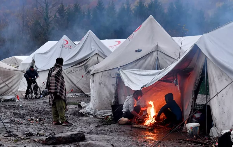 Illegal migrants stand near a fire under a tent, on November 20, 2019, at "Vucjak" camp, in the outskirt of the city of Bihac, in northern Bosnia. - Caught in the "limbo" between local and international politics, migrants remain stuck at this improvised camp, in inadequate living conditions, between attempts to illegally enter the EU territory in neighboring Croatia. Living conditions at the camp have deteriorated past the brink of a health hazard in recent days, meals are scarce, medical care is limited to emergencies while winter has almost arrived and Bosnian central government although helped from the EU, doesn't have neither plan nor capacity to handle the crisis. (Photo by ELVIS BARUKCIC / AFP)