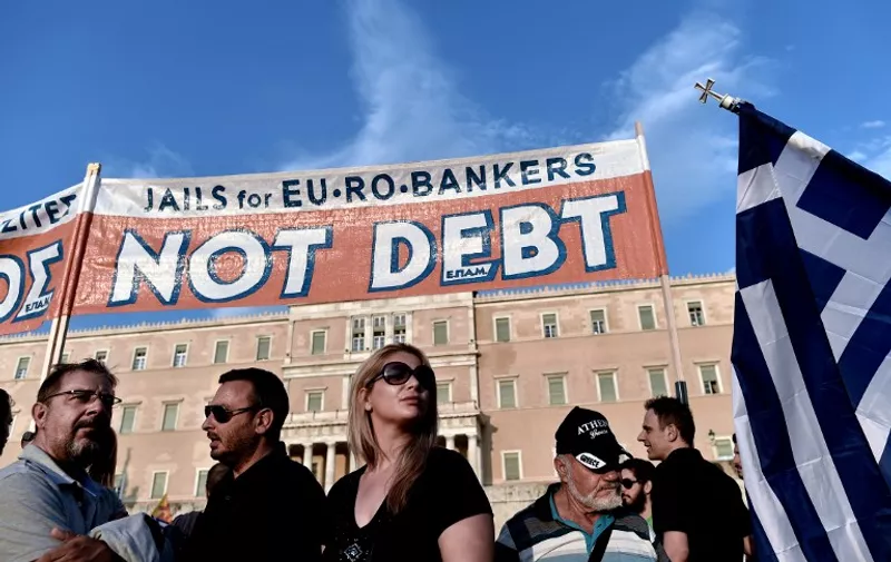 Prostestors stand below a banner reading ''No Debt''  in reference to the forthcoming  referendum on bailout conditions set by the country's creditors, during a demonstration in front of the Greek parliament in Athens on June 29, 2015.  Greece shut its banks and the stock market and imposed capital controls after creditors at the weekend refused to extend the country's bailout past the June 30 deadline, prompting anxious citizens to empty ATMs.  AFP PHOTO /  ARIS MESSINIS