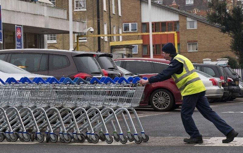 A worker pushes a line of trolleys in the car park at a branch of Tesco in south London, on January 9, 2018. (Photo by Justin TALLIS / AFP)