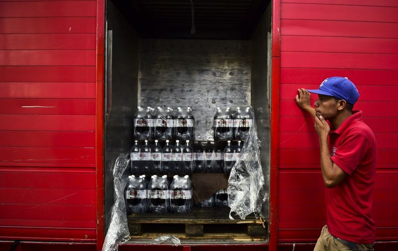 A worker stands next to bottles of Coca Cola that he is unloading from a truck in Caracas on May 27, 2016. - Coca Cola suspended much of its distribution in Venezuela due to a shortage of sugar. (Photo by RONALDO SCHEMIDT / AFP)