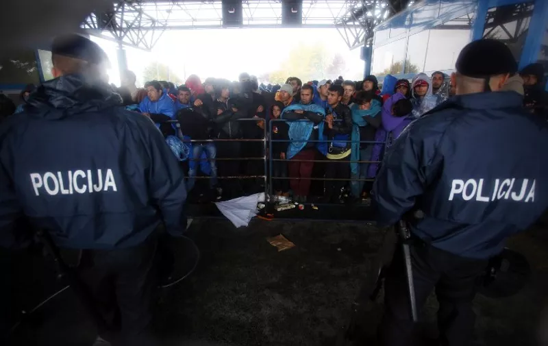 Croatian policemen stand in front of migrants who try to protect themselves from the rain on October 19, 2015 at the Croatian-Slovenian border crossing in Trnovec. Slovenian authorities said today they had refused to let in more than 1,000 migrants arriving from Croatia after a daily quota had been reached, stoking fears of a new human bottleneck on the western Balkan route. The desperate refugees and migrants were forced to spend the night in freezing temperatures near rail tracks after police stopped them from walking across the border dividing the two EU states.  AFP PHOTO/STRINGER