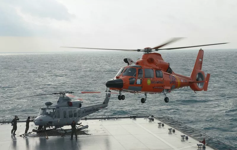 An Indonesian search and rescue helicopter (R) prepares to land on the Indonesian Navy vessel KRI Banda Aceh as operations to lift the tail of AirAsia flight QZ8501 continue in the Java Sea on January 9, 2015. Ping signals from the black box data recorders of crashed AirAsia Flight QZ8501 were detected on January 9, a senior Indonesian search official told AFP.      AFP PHOTO / POOL / ADEK BERRY (Photo by ADEK BERRY / POOL / AFP)